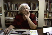 Janet Jagan, in her 80s, sitting in her desk behind a manual typewriter and in front of a bookshelf.
