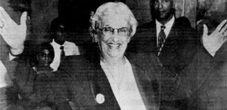Janet Rosenberg Jagan, now older, as the president of Guyana, smiling and holding her hands up in victory.