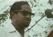 Forbes Burnham giving a speech at a podium, wearing dark sunglasses.